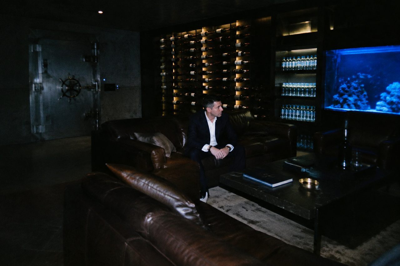 A billionaire's underground bunker lounge: steel blast door, leather sofas, a wall of wine and shelves of bottled water