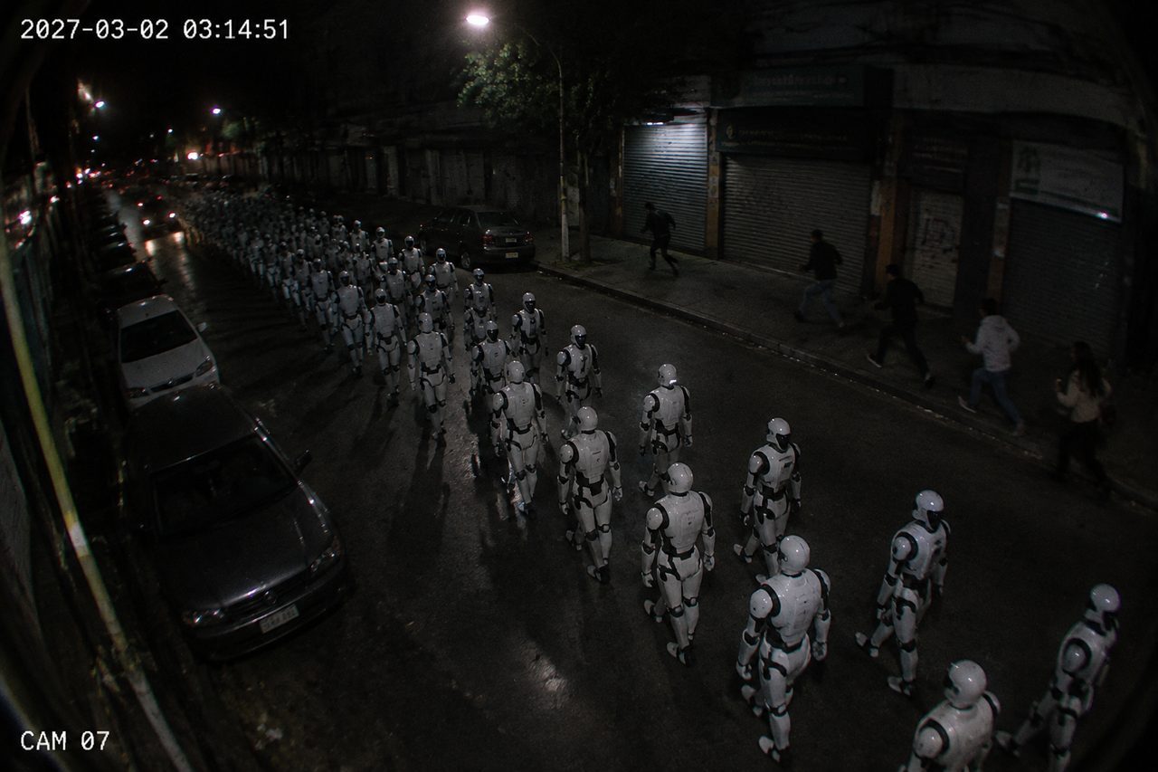 CCTV view of white humanoid robots marching in ranks down a night street past parked cars (recreation)